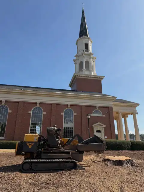 Tracked grinder on the lawn in front of a brick church with a white steeple