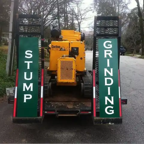 Yellow tracked grinder on the trailer between green STUMP and GRINDING loading ramps